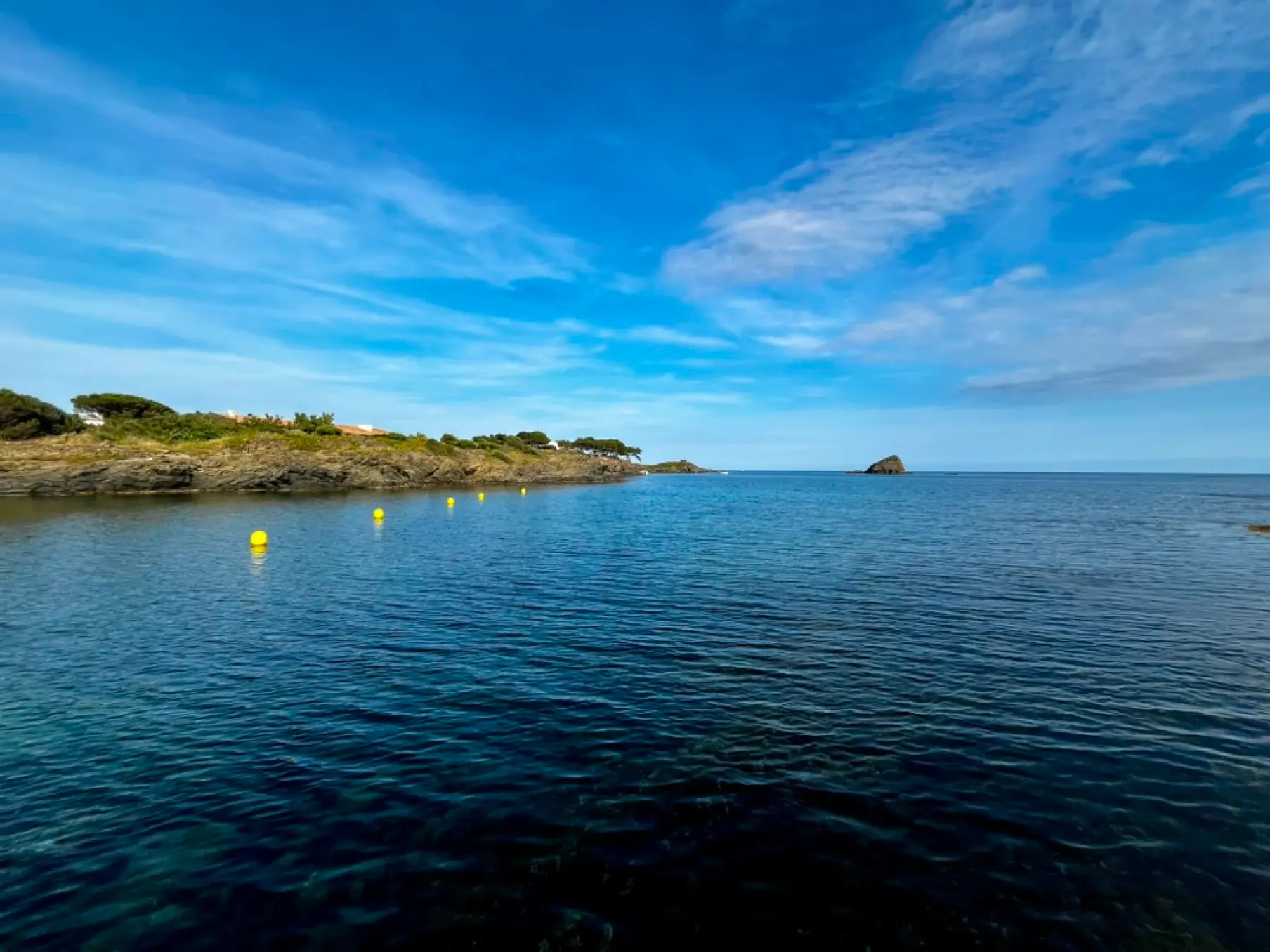 Calm crystal clear waters with rocky coastline and yellow buoys at Platja d'en Pere Fet, Cadaqués