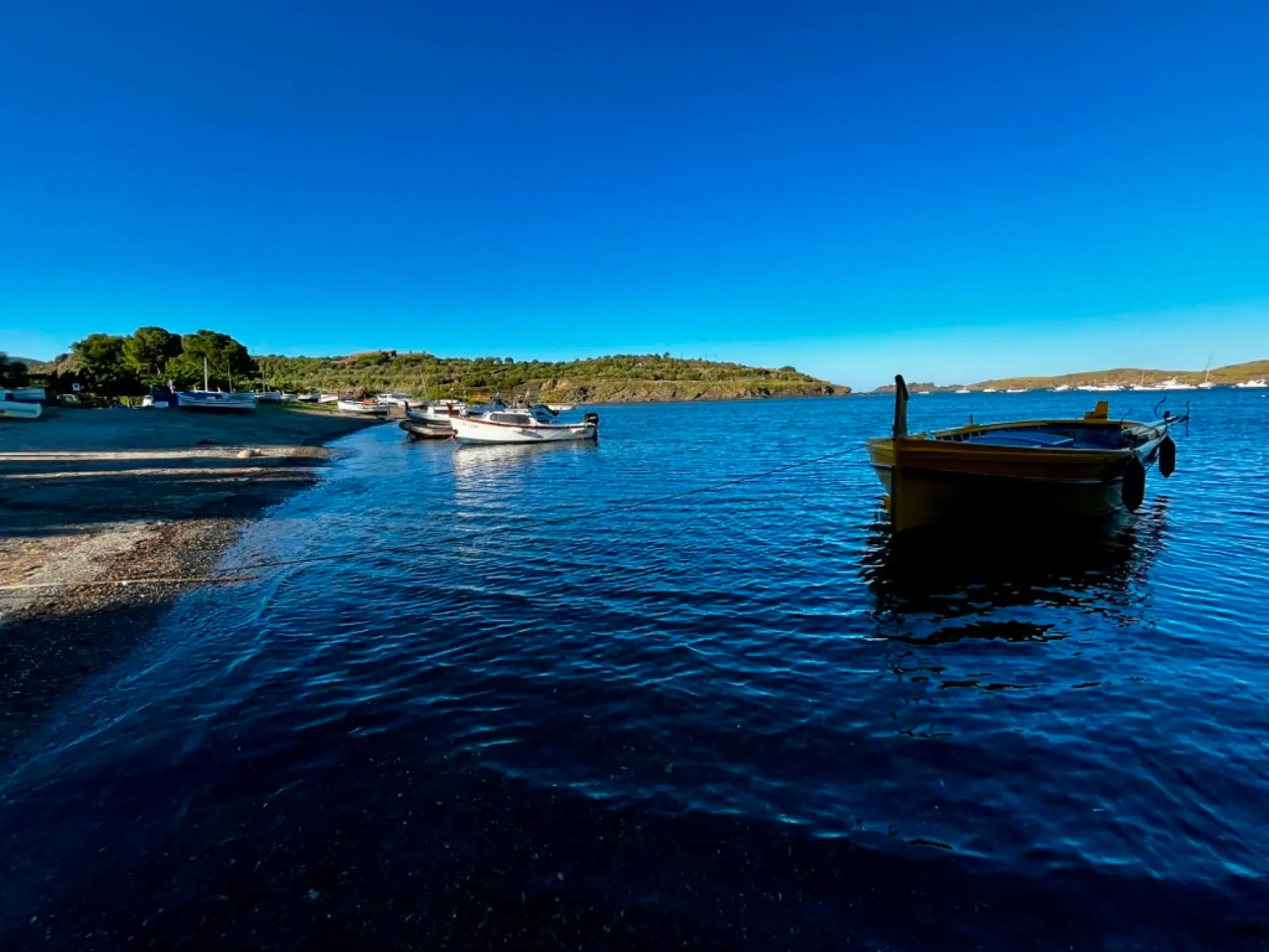 Calm turquoise waters of Portlligat bay with anchored boats facing Salvador Dalí House Museum, Cadaqués